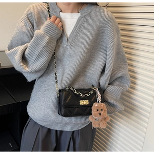 Detail of black quilted leather crossbody bag with gold chain and plush bear charm
