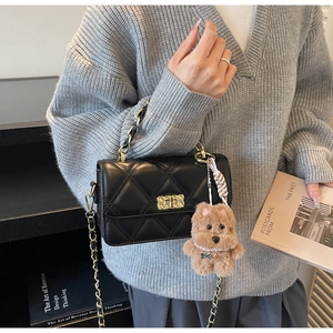 Detail of black quilted chain bag with gold twist lock and brown plush bear charm