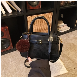 Détail du sac seau noir tissé avec boucle dorée et accessoire décoratif en pompon doux