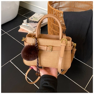 Detailed close-up of woven light coffee bucket bag with gold hardware and plush fur ball charm