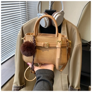 Detail of khaki bucket bag with woven texture, metal buckle and decorative plush pom-pom