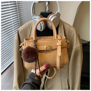 Detail of earth-tone textured bucket bag with leather strap and fur pompom accessory