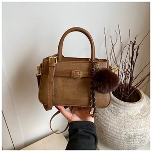 Detail view of brown woven bucket bag featuring gold buckle and plush pompom charm