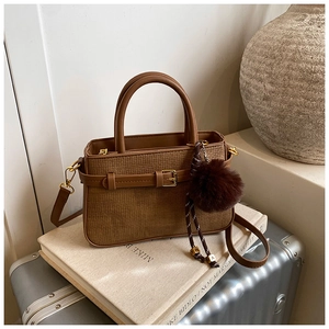 Detailed view of brown woven bucket bag with leather accents and plush charm on a suitcase