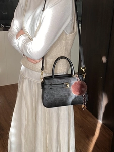 Sac seau tissé noir avec boucles dorées et pompon rose pour un style sophistiqué