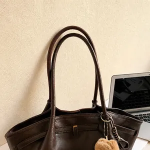 Dettaglio del manico in pelle di borsa a secchiello marrone retrò con ciondolo morbido