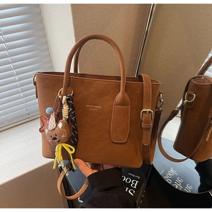 Gros plan du sac seau en daim marron avec détails dorés et porte-clés ours décoratif