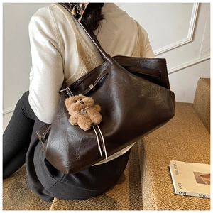 Detail of dark brown leather bucket bag with cute plush bear charm on a shoulder strap