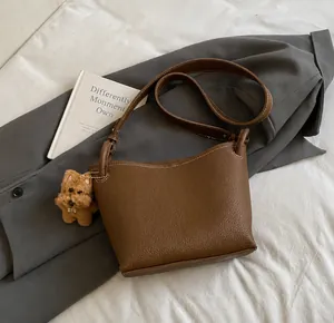 Détail du sac seau en cuir grainé marron foncé avec un joli pendentif ours en peluche