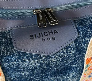 Macro view of blue denim fabric tote bag with grey leather accents and dual metal zippers