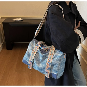 Detail of blue denim tote bag featuring colorful floral embroidered strap and leather corners