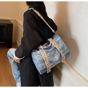 Detail of blue denim tote bag featuring decorative floral embroidery on the shoulder strap