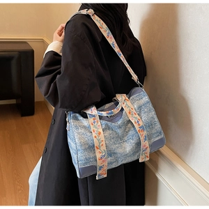 Detail of blue denim tote bag with colorful ethnic floral embroidery and purple leather base