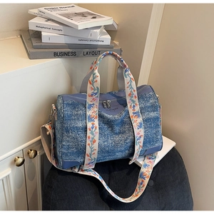 Detail of blue denim textured Boston bag featuring colorful floral embroidered strap