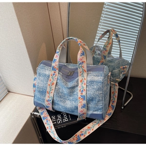 Close-up of a blue denim Boston bag featuring intricate floral embroidery on the handles