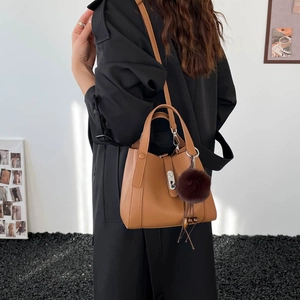 Detail of tan lychee leather bucket bag with purple pompom and silver metal lock on model