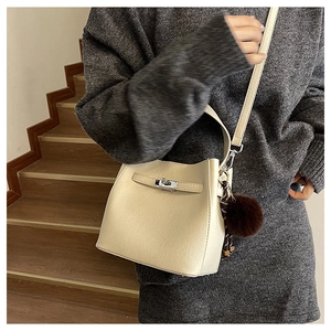 Detail van beige emmertas met zilveren draaisluiting en zachte pluche bal als accessoire