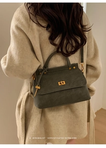 Detail of retro dark green suede handbag with gold lock and key charm on beige coat