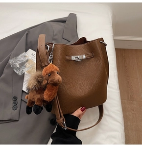 Detail of warm brown pebbled leather bucket bag with silver twist-lock and camel charm