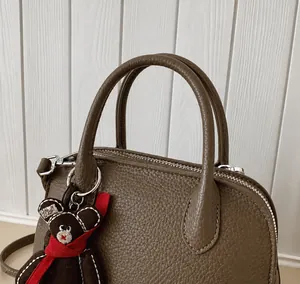 Detail showing reinforced double handles and a cute bear charm on a brown leather bag