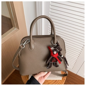 Detail of dark brown lychee leather shell bag with cute plush bear charm on wooden stand