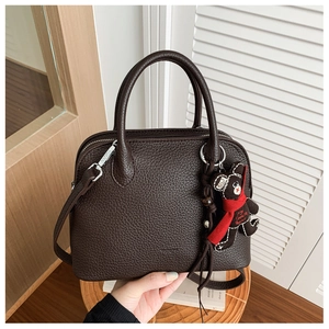 Macro detail of dark brown litchi grain leather handbag with cute plush bear charm