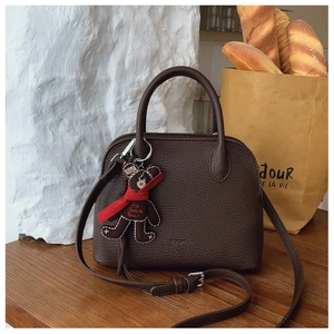Detail view of dark brown pebbled leather shell bag with a cute bear charm and silver hardware