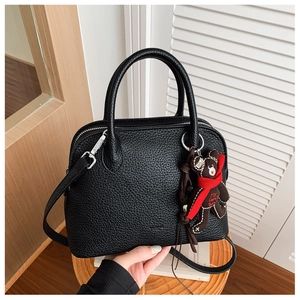 Close-up of black litchi pattern handbag with cute bear charm and silver hardware