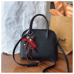 Detail of black litchi grain leather handbag with brown plush bear charm on wooden table