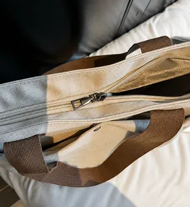 Close-up of smooth metal zipper detail on a beige canvas tote bag with woven strap