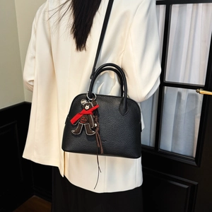 Detail view of black lychee grain leather shell bag with a cute bear charm and shoulder strap