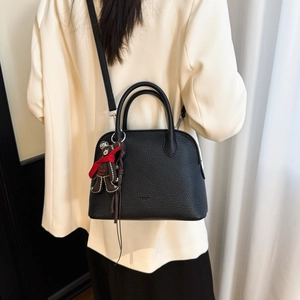 Detail of black pebbled leather shell bag with a brown bear pendant and crossbody strap