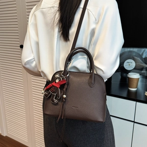 Detail of dark brown lychee leather shell bag with bear charm worn by a model