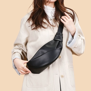 Close-up of stylish black crescent crossbody bag with pleated texture and knotted strap