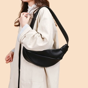 Detail of black glossy leather crescent bag with cross-fold texture and knotted strap