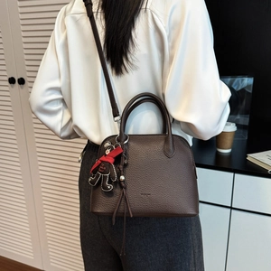 Detail of dark brown pebble leather shell bag with cute teddy bear charm accessory