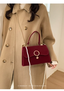 Detail of a deep red velvet wedding handbag with gold hardware and white pearl strap