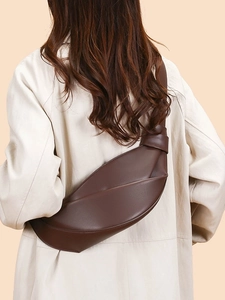 Dark brown leather croissant shoulder bag with pleated design on female model in trench coat
