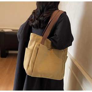 Detail view of mustard canvas tote bag with front pocket and wide brown shoulder strap