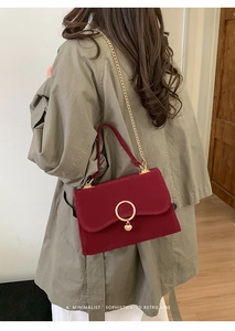 Detail view of burgundy velvet handbag with gold heart pendant worn on a long grey coat