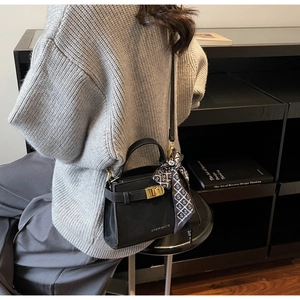 Détail d'un sac à main en cuir noir avec un foulard en soie et un fermoir doré