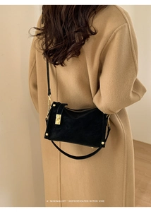 Detail of a black retro shoulder bag with gold clasp shown on a camel coat outfit