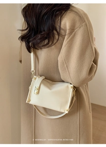 Detail of a creamy white underarm bag with litchi texture and golden metal accents