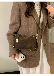 Close-up of retro brown suede shoulder bag with gold hardware and rivet detailing