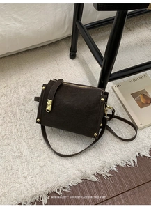 Detail view of vintage dark brown crossbody bag with gold rivets and smooth zipper