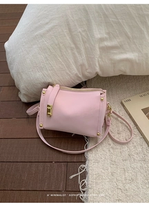 Detailed view of pink shoulder bag with gold zipper and vintage buckle on wood floor
