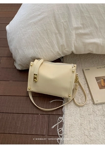 Detailed macro view of the cream-colored matte leather crossbody bag with golden hardware