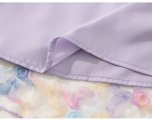 Detailed close-up of lavender girl dress hem with colorful floral mesh embroidery layer
