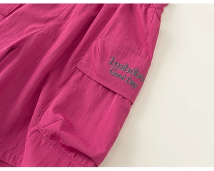 Detail of rose red cargo shorts showing utility pocket and embroidered letter patch