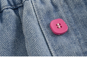 Dettaglio del denim azzurro con bottone quadrato rosa acceso ed elastico in vita morbido